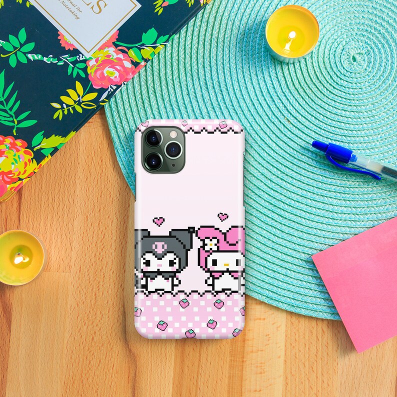Puede incluir: Una funda de tel&eacute;fono rosa y blanca con un dise&ntilde;o pixelado de dos personajes de dibujos animados. Los personajes son un gato blanco y negro con un lazo y un conejo rosa con un lazo. La funda tiene un patr&oacute;n de cuadros rosa y blanco con fresas rosas.