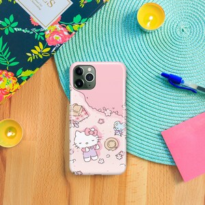 May include: A pink phone case with a Hello Kitty design. The case features Hello Kitty laying down on a pink background with flowers and a small mouse.