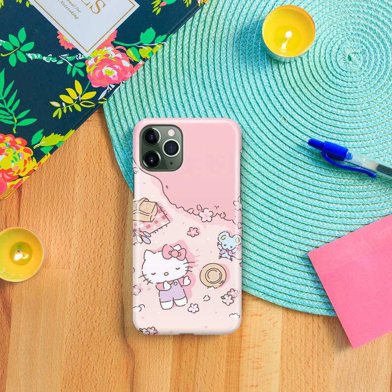 May include: A pink phone case with a Hello Kitty design. The case features Hello Kitty laying down on a pink background with flowers and a small mouse.