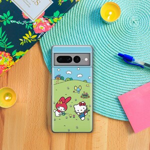 Puede incluir: Una funda transparente para tel&eacute;fono con un dise&ntilde;o de dibujos animados coloridos que presenta a Hello Kitty y My Melody haciendo jardiner&iacute;a en un campo verde. La funda tiene un fondo de cielo azul con nubes blancas.