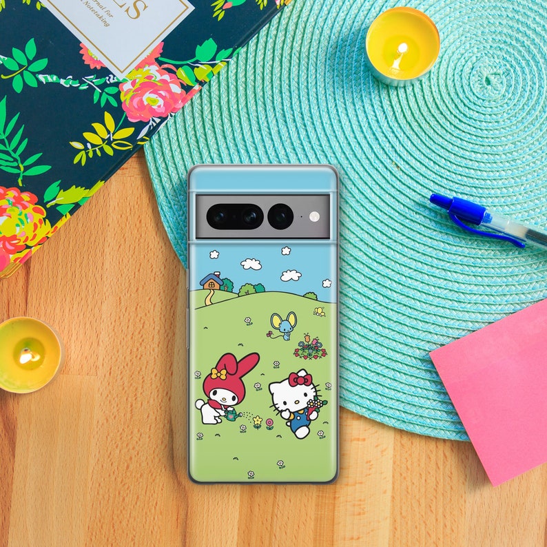 Puede incluir: Una funda transparente para tel&eacute;fono con un dise&ntilde;o de dibujos animados coloridos que presenta a Hello Kitty y My Melody haciendo jardiner&iacute;a en un campo verde. La funda tiene un fondo de cielo azul con nubes blancas.