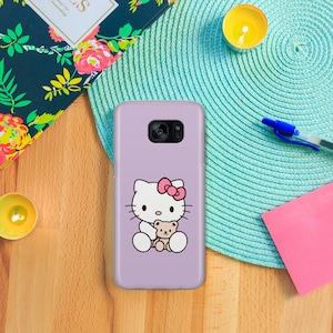 May include: A lavender phone case featuring a white Hello Kitty character holding a brown teddy bear. Hello Kitty has a pink bow on her head.