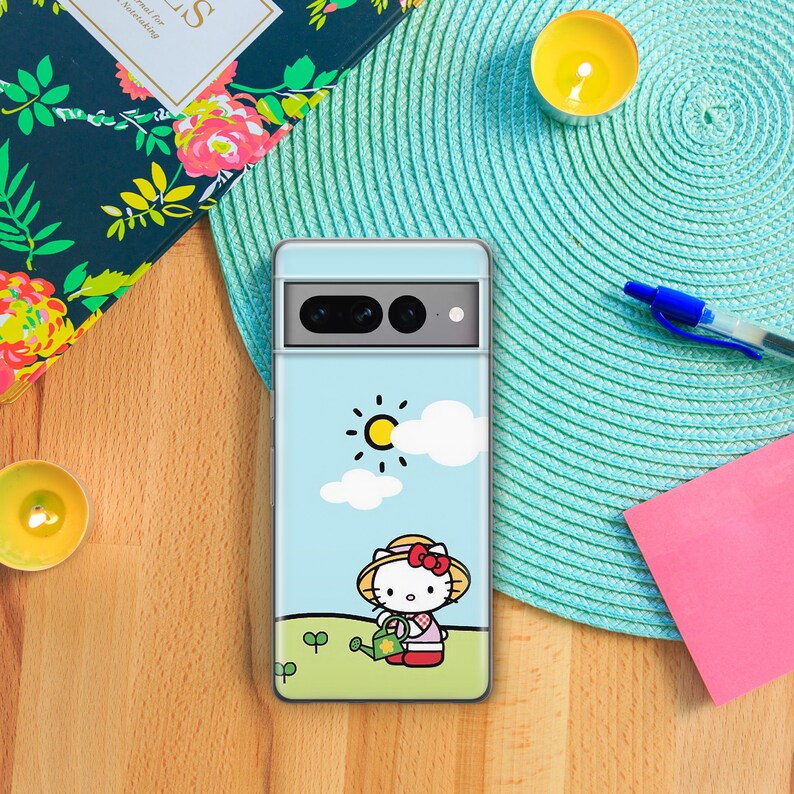 Puede incluir: Una funda de tel&eacute;fono azul con una imagen de dibujos animados de Hello Kitty regando plantas en un campo soleado. La funda tiene un recorte para la c&aacute;mara del tel&eacute;fono.