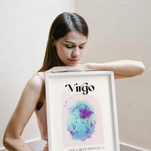May include: A white framed print with a watercolor illustration of a Virgo zodiac sign. The illustration is in shades of blue, pink, and purple. The text "Virgo" is in black and the text "The Earth Witch" is in black below the illustration.
