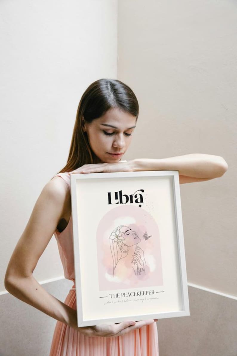 May include: A white framed print featuring a pink and white watercolour illustration of a woman with a butterfly. The text "Libra" and "The Peacekeeper" is printed in black.