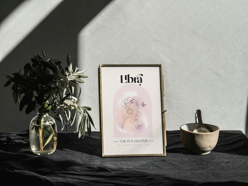 May include: A gold framed print with the word "Libra" in a stylised font. The print features a watercolour illustration of a woman with a butterfly. The text "The Peacekeeper" is below the illustration.