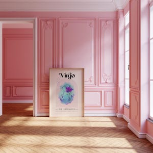 May include: A framed print with the word "Virgo" in a stylized font. The print features a watercolor illustration of a woman with flowers and the text "The Earth Witch". The print is hanging on a pink wall in a room with white trim.