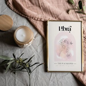 May include: A gold framed print with the word "Libra" in black text. The print features a watercolour illustration of a woman with flowers in her hair and a butterfly. The text "The Peacekeeper" is below the illustration.