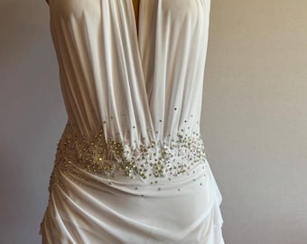May include: White halter dress with a plunging neckline and a beaded embellishment around the waist.