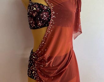 May include: A dance costume with a red-orange sheer overlay and a black sequined bodice. The costume features a cutout design and is adorned with small, scattered embellishments. The fabric drapes elegantly, creating a flowing silhouette.