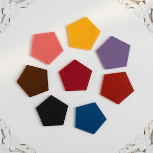 May include: A collection of eight pentagon-shaped felt pieces arranged in a circular pattern. The colours include yellow, purple, red, blue, black, brown, pink, and a central dark red piece, all featuring a textured, soft fabric surface.