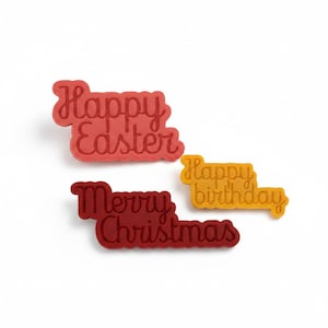 Op de afbeelding: Drie platte, decoratieve plaatjes met reliëftekst. Eén rood plaatje leest Happy Easter, één donkerrood plaatje leest Merry Christmas en één geel plaatje leest Happy birthday. Elk stuk heeft een ontwerp met afgeronde randen.