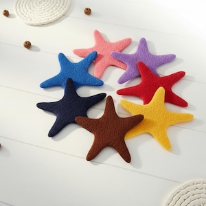 Puede incluir: Un conjunto de siete formas de estrella de mar de lana fieltrada en varios colores, incluyendo rosa, morado, azul, azul oscuro, marrón, rojo y amarillo. Cada estrella de mar tiene una superficie texturizada y difusa con cinco brazos.