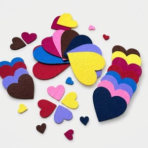 May include: A collection of felt heart cutouts in various sizes and colours, including yellow, pink, red, blue, purple, and brown. The hearts are arranged in clusters and scattered individually across the frame, showcasing a flat, textured surface.