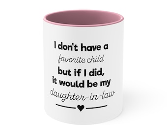 May include: White ceramic coffee mug with a pink rim. The mug has black text that reads "I don't have a favorite child but if I did, it would be my daughter-in-law" with a small black heart underneath.
