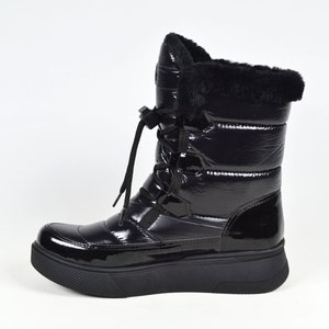 May include: Black winter boots with a shiny patent leather finish and a thick platform sole. The boots have a lace-up front and a faux fur trim around the top.