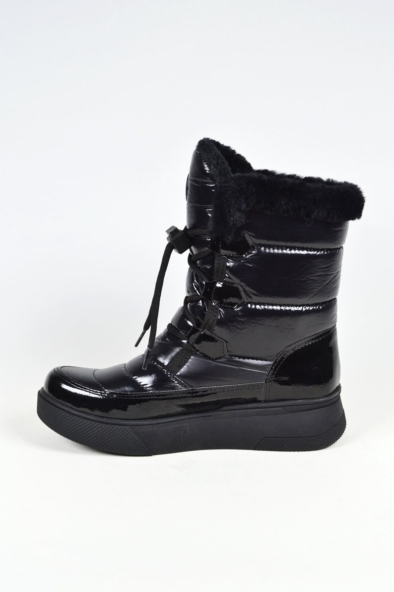 May include: Black winter boots with a shiny patent leather finish and a thick platform sole. The boots have a lace-up front and a faux fur trim around the top.