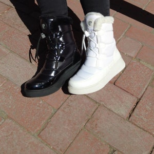 May include: A pair of winter boots, one black and one white, with a puffy design and laces. Both boots have a faux fur trim around the top.