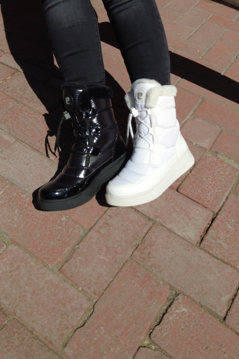 May include: A pair of winter boots, one black and one white, with a puffy design and laces. Both boots have a faux fur trim around the top.