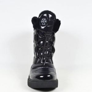 May include: Black quilted winter boots with a faux fur trim around the top and a black lace-up closure. The boots have a black logo on the side.