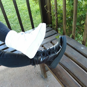 May include: A pair of black and white boots with laces. The black boot is on the right foot and the white boot is on the left foot. The boots are worn by a person sitting on a wooden bench.