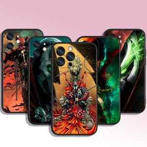 May include: Five black phone cases featuring comic book artwork. The designs showcase Spawn characters in action poses, using red, green, black, and gold. The cases have a glossy finish and are set against a pink backdrop.