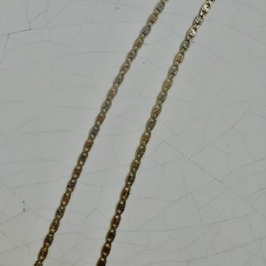 May include: Two gold chains with a textured, patterned design. The chains are laid out parallel to each other on a white surface.