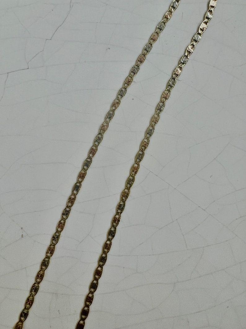 May include: Two gold chains with a textured, patterned design. The chains are laid out parallel to each other on a white surface.