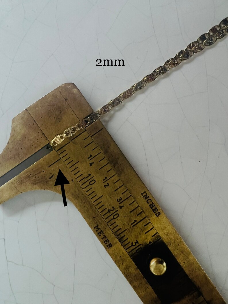 May include: Close-up of a gold chain measured with a ruler. The chain is 2 mm wide.  The ruler shows inches and millimeters.