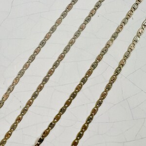 May include: Three gold chains with a textured, patterned design. The chains are laid out in parallel lines on a white surface.