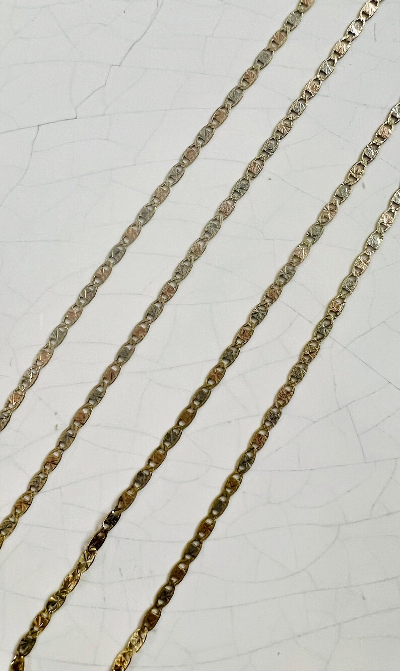 May include: Three gold chains with a textured, patterned design. The chains are laid out in parallel lines on a white surface.