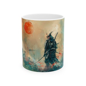 May include: White ceramic mug featuring a watercolor illustration of a samurai warrior in black armor with a sword, set against a backdrop of a red sun and a muted, artistic landscape. The design has a painterly style.