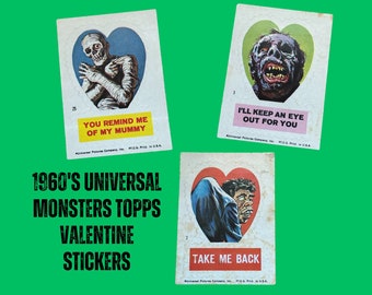 May include: Three vintage Valentine's Day stickers featuring Universal Monsters characters. The stickers are red, white, and black with images of the Mummy, the Creature from the Black Lagoon, and Dracula. The text on the stickers reads "You remind me of my Mummy", "I'll keep an eye out for you", and "Take me back".