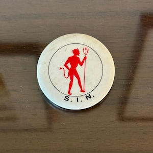 May include: A circular white pinback button featuring a red silhouette of a devil holding a trident inside a thin black circular border. The letters S. I. N. are printed in black capital letters at the bottom of the circular design.
