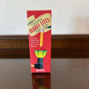 May include: A red box featuring a Christmas Bubble Lites Night Light. The box has text that reads "Bubbling Night Light reflects the spirit of the Holiday." The night light has a yellow bubbling tube and a green and red base.