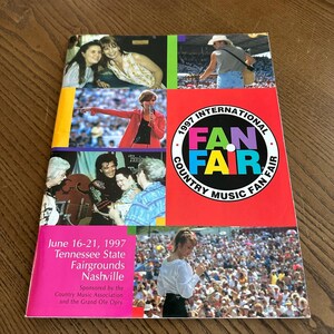 May include: A vintage 1997 International Fan Fair Country Music Fan Fair program. The cover features images of country music performers and the event's logo. The program's dates and location are also displayed.