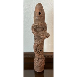 Puede incluir: Flauta de arcilla marrón tallada a mano. Presenta una serpiente tallada enrollada alrededor del cuerpo, con una cara detallada en la parte inferior. La parte superior tiene un agujero y anillos decorativos.