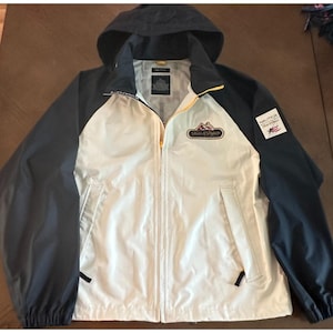 May include: A Nautica hooded jacket in white, navy blue, and yellow. The jacket has a zip-up front, two pockets, and a logo patch on the sleeve. The jacket has a logo on the chest that says "Ski & Snow".