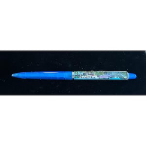 May include: A blue pen with a clear barrel and a scenic image of a bridge and buildings. The pen has a blue tip and a blue end cap. The pen is on a black surface.