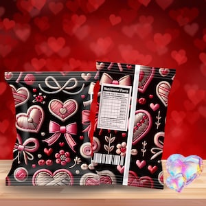 Op de afbeelding: Twee zwarte snackzakken met roze geborduurde harten, strikken en bloemmotieven. Eén zak toont een voedingswaardelabel. De achtergrond is een wazig rood met hartvormen. Op een houten oppervlak.