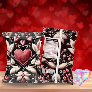 Op de afbeelding: Twee decoratieve snackzakken met een Valentijnsdagthema. De zakken zijn zwart met een hartontwerp in het midden, omgeven door witte bladeren en roze accenten. Eén zak zit vooraan en de andere erachter. Rechts ligt een hartvormig kristal.