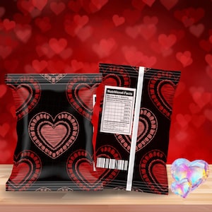 Op de afbeelding: Twee zwarte snackzakken met een herhalend patroon van rode geborduurde harten. Eén zak heeft een voedingsetiket en een barcode. De achtergrond is een wazig rood met hartvormen. Een houten oppervlak is op de voorgrond.