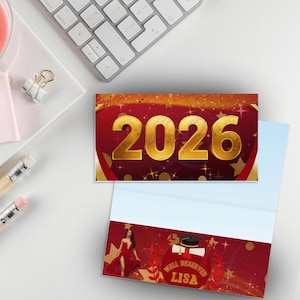 May include: A graduation card with the year 2026 in gold lettering on a red background with gold stars. The card is open, revealing a woman in a red dress and the text "Well Deserved Lisa". Pencils, a paper clip, and a keyboard are also visible.