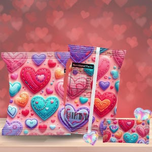 Op de afbeelding: Roze snackzakken met een hartpatroon in verschillende kleuren, waaronder rood, blauw en paars. De zakken hebben een gestikt ontwerp en een voedingswaardelabel. Een kleine candybar met een hartontwerp is ook zichtbaar.