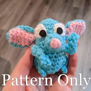May include: A crocheted blue and pink mouse amigurumi toy. The mouse has large black eyes and a pink nose.