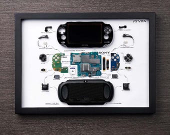 Puede incluir: Un marco negro muestra una PlayStation Vita desmontada, revelando sus componentes. El fondo blanco destaca las piezas, incluyendo la pantalla, botones y placa base, con etiquetas. El logotipo de PlayStation Vita es visible.