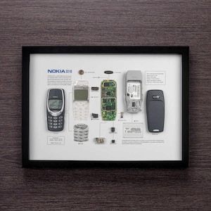 May include: A framed infographic showing the disassembled parts of a Nokia 3310 mobile phone. The infographic includes a diagram of the phone's internal components, as well as a list of the phone's specifications. The phone is shown in its entirety, as well as in its disassembled state.