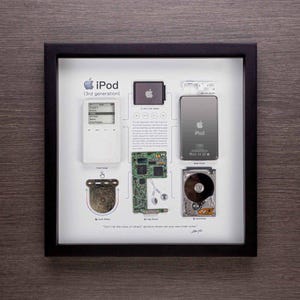 May include: A framed display showing the disassembled parts of a white 3rd generation iPod. The display includes the iPod's front cover, touch wheel, logic board, 2-inch LCD screen, hard drive, and back cover. The text "iPod (3rd generation)" and "Don't let the noise of others' opinions drown out your own inner voice." is included in the display.