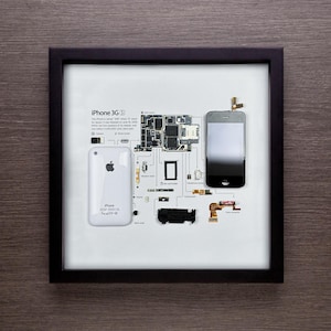 May include: A framed print of a disassembled iPhone 3G, showing the individual components and their placement within the phone. The print includes a description of the phone and its features, including the text "iPhone 3G (S)".