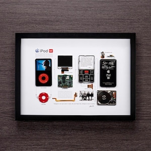 May include: A framed display of the disassembled parts of an iPod U2 special edition, including the hard drive, screen, and circuit board. The display also includes a quote from Jony Ive, "Design is not just what it looks like and feels like. Design is how it works."